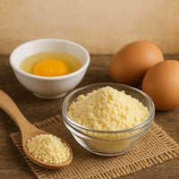 Powdered eggs in a glass bowl with whole eggs and raw egg in a white bowl on a wooden table