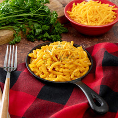 Cheesy macaroni in skillet with shredded cheese, parsley, and red checkered napkin
