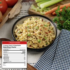 A bowl of creamy pasta and vegetable medley with peas and bacon bits, styled with celery, carrots, parsley, and tomatoes on a tablecloth. A product label overlay in the lower left reads 'Creamy Pasta & Vegetable Nutrition Facts' and says '1 Pouch Included.