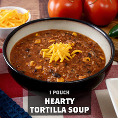 Bowl of hearty tortilla soup with cheddar cheese, tomatoes, and soup ingredients on table.