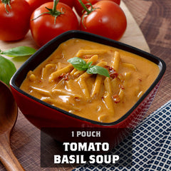 Tomato basil soup in a red bowl with fresh tomatoes and basil on a wooden table